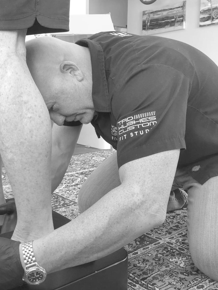 Tad Hughes kneeling to assess a client's foot and ankle position in his fitting studio
